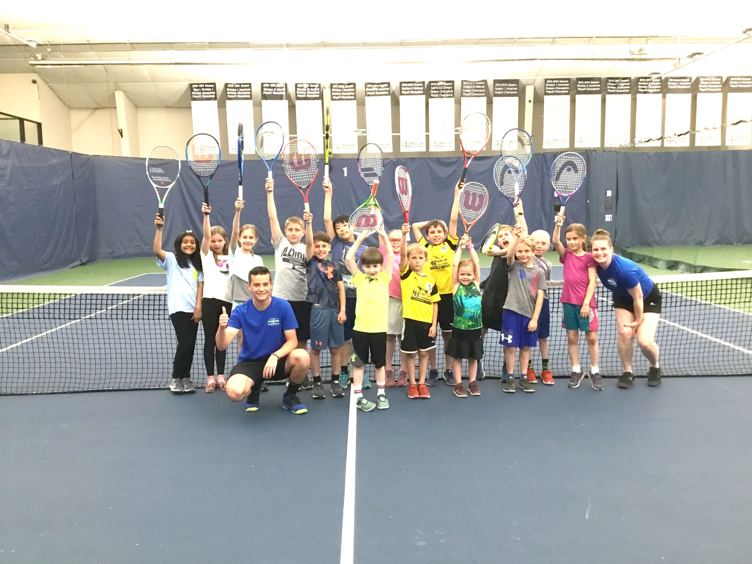 Wheaton Sport Center kids on tennis court holding up their rackets at Tennis Evolution Camp